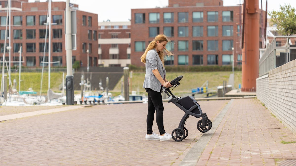 Woman pushing a rollator walker on a smooth paved urban path in summer