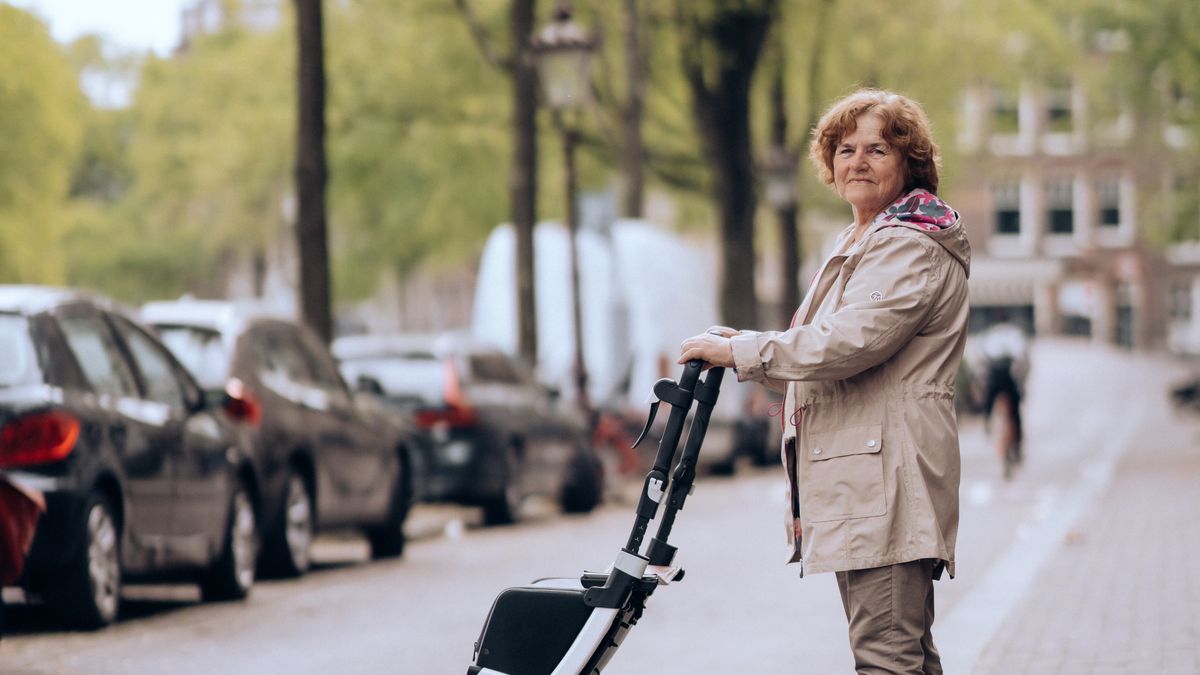 Senior woman using a rollator walker on a tree-lined sidewalk in summer